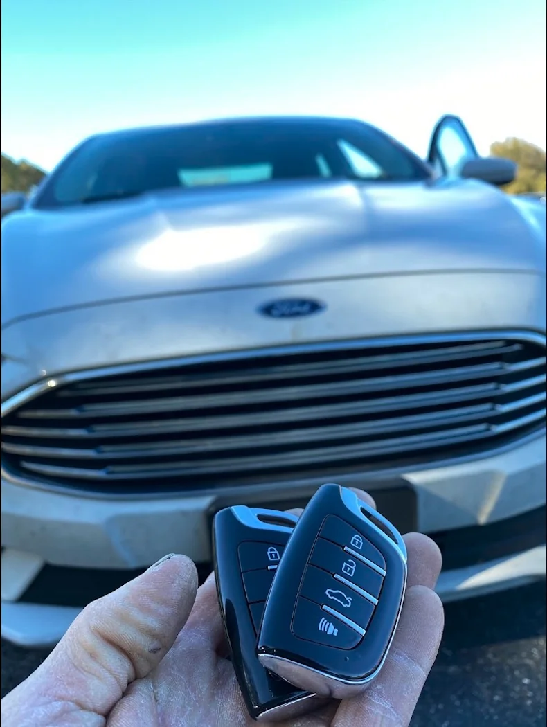 Two Ford key fobs held in front of a silver Ford car