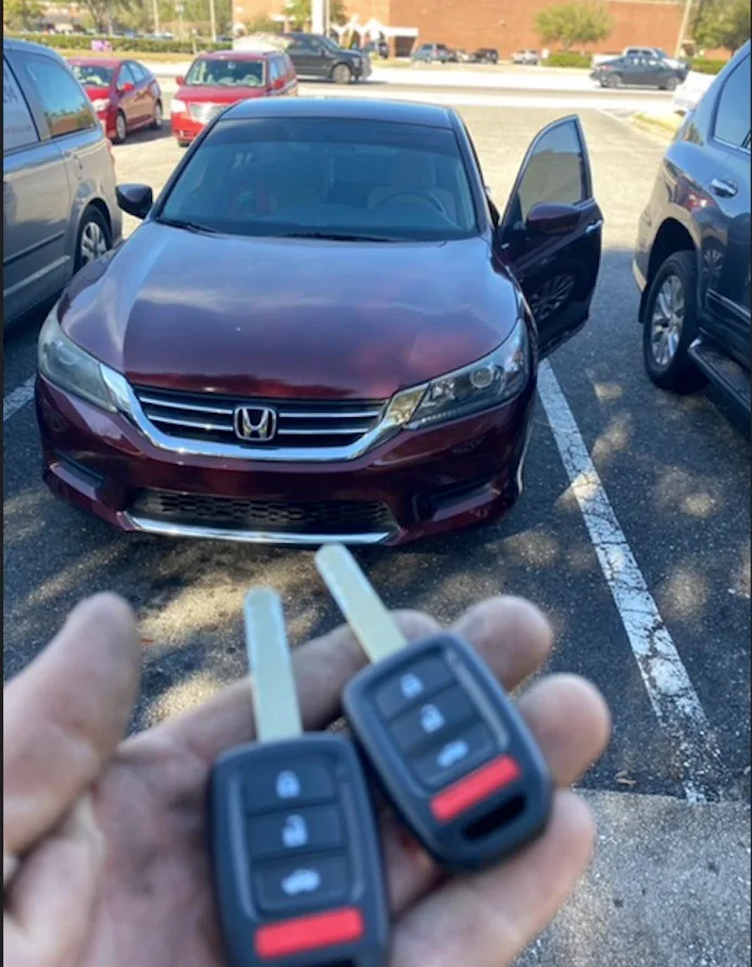 Two Honda remote keys held in front of a burgundy Honda car